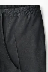 Pantalón tipo jogger de vestir con pliegues frontales y traseros, cintura elástica con cordón de ajuste, bolsillos laterales al bies y bolsillos traseros insertados. Presenta un corte slim fit entallado.