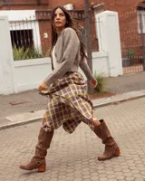 Botas de caña alta confeccionadas en cuero gamuzado color marrón. Presentan un diseño de estilo western con puntera cuadrada, taco de madera y una tira decorativa con estribo metálico desmontable en la zona del tobillo.