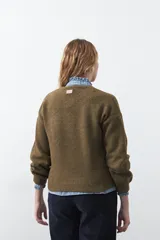 Sweater de tejido suave color tostado, con cuello redondo y detalle de flores bordadas en relieve en la parte superior del pecho. Presenta un corte relajado y mangas largas con puños ajustados.