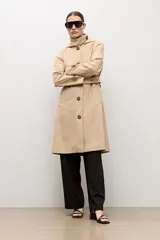Trench clásico color beige, con cuello alto, capucha desmontable, cierre frontal de botones marrones, bolsillos ribeteados y cinturón ajustable con hebilla.