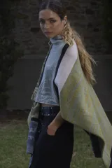 Ruana tejida en lana lambswool con diseño de bloques de color y tramas geométricas. Presenta cierre frontal con doble cursor y tiradores de cuero, permitiendo diferentes formas de uso.