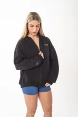 Campera con cierre frontal metálico, confeccionada en algodón pesado de alto gramaje. Presenta un diseño oversize con capucha, bolsillos tipo canguro y bordados minimalistas en el frente y en la manga.