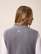 Chaleco de tejido de punto en color gris, con cierre frontal completo, cuello alto y dos bolsillos delanteros tipo parche.