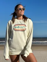 Buzo color crema de algodón con cuello redondo y mangas largas. Estampado en el frente con líneas horizontales de colores y una línea ondulada que simula un electrocardiograma.