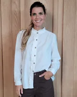 Camisa de algodón con cuello mao y volados sutiles a lo largo de la botonadura frontal. Presenta mangas largas con puños abotonados y detalle de frunces en los hombros.
