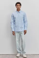 Camisa de vestir de manga larga en color celeste claro, con cuello clásico y cierre frontal de botones. Presenta un corte recto y un diseño minimalista.