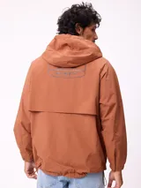 Campera impermeable Rusty con capucha, confeccionada en nylon. Presenta cierre frontal con botones a presión, bolsillos delanteros con solapa y puños elásticos.