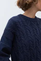Sweater de punto trenzado en color azul marino, con cuello redondo y mangas largas. Presenta un diseño de tejido con textura en el frente y mangas lisas.