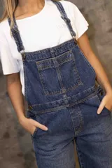 Enterito de denim azul con silueta relajada, breteles regulables, peto con bolsillo frontal y piernas rectas con tajos laterales en el ruedo.