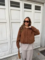 Campera de estilo bomber confeccionada en simil gamuza color marrón, con cuello camisero, cierre frontal oculto y puños elásticos.