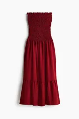 Vestido midi strapless de color bordó, con cuerpo fruncido elástico y falda larga acampanada con un volante en el bajo.
