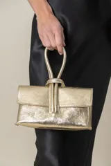 Cartera de mano dorada de cuero laminado, con lazo en el asa y correa desmontable para colgar.