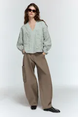 Blusa de escote pico y manga larga con puño elástico y volante. Presenta un diseño de rayas verticales finas en azul claro y blanco, con flores en relieve.