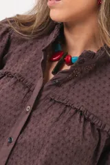 Camisa de broderie color marrón chocolate, con cuello alto, detalles de volados, mangas largas abullonadas y cierre frontal de botones.