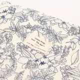 Necesér acolchado con estampado floral en azul sobre fondo blanco, cierre de cremallera y etiqueta con texto.