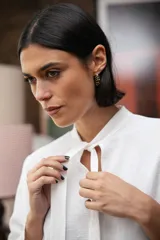 Blusa blanca de textura arrugada, con cuello alto, abertura frontal tipo gota y mangas largas acampanadas con detalle de frunces.