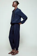 Pantalón de tiro alto de tela satinada color azul marino, con bolsillos frontales, cintura ajustable con cordones y puños elásticos en los tobillos.