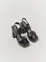 Sandalias de plataforma con taco cuadrado alto, confeccionadas en cuero metalizado color dorado. Presentan un diseño de tiras anchas cruzadas en el empeine y cierre con pulsera al tobillo.