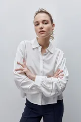 Camisa de viscosa blanca con calce amplio, cuello clásico, mangas largas con puños abotonados y detalles de calados lineales en el frente y las mangas.
