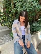 Camisa de tejido de punto con diseño de rayas horizontales en tonos gris y beige. Presenta cuello clásico, cierre frontal con botones y bolsillos delanteros con detalles en cuero metalizado.