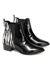 Bota tipo chelsea con diseño combinado. Presenta la parte delantera en cuero vacuno charolado negro y la parte trasera en cuero con estampado animal print tipo cebra. Cuenta con elásticos laterales negros y taco cuadrado bajo.