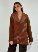 Saco de lana color verde militar con estampado abstracto en tonos verde oliva y detalles bordados en rojo. Tiene cuello solapa, cierre frontal con botones de madera y puños acanalados.