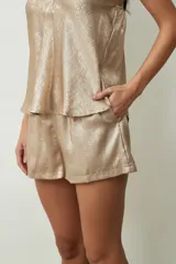 Short de tiro medio en color dorado con acabado metalizado, diseño holgado y bolsillos laterales.