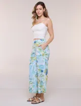 Pantalón crop de lino y rayón, con diseño wide leg de corte holgado, estampado tropical de hojas en tonos verde, azul y marrón sobre fondo blanco. Cuenta con pretina trasera elastizada y bolsillos delanteros.