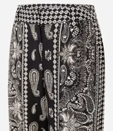 Pantalón largo de corte ancho con estampado paisley en tonos blanco y negro. Presenta cintura alta con trabillas, cierre frontal tradicional y confección en tejido viscolino, una mezcla de lino y viscosa.
