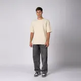 Remera oversized de algodón grueso con textura micropanal, color beige, de cuello redondo y manga corta, con costura decorativa en "X" en el escote y diseño liso sin logos.