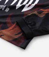 Remera de manga larga con corte boxy, confeccionada en microfibra de poliéster. Presenta un diseño estampado con motivos de llamas en tonos rojos y naranjas, junto con el número 13 en tipografía gótica en la espalda.