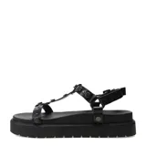 Sandalias planas Miss Carol estilo flatform, color negro con tachas metálicas en las tiras y suela chunky acanalada. Cuenta con cierre de hebilla ajustable en el tobillo.