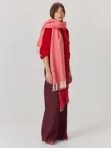 Bufanda de gran tamaño en color mostaza con diseño de tejido en espiga y flecos en los extremos. Incluye una etiqueta metálica decorativa en una de las esquinas.