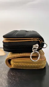 Billetera corta de diseño capitoneado con cierre perimetral y solapa frontal. Cuenta con compartimentos internos para tarjetas y billetes, e incluye una correa de mano desmontable.