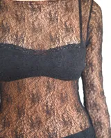 Vestido corto de encaje negro con diseño asimétrico en el ruedo. Presenta mangas largas y un corte ajustado, con un estilo que combina transparencia y texturas.
