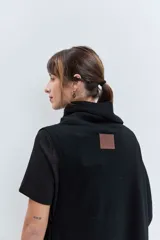 Poncho asimétrico de tejido de punto en color marrón, con cuello alto tipo polera y diseño sin mangas con aberturas laterales.