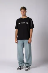 Remera de algodón color blanco con corte regular, cuello redondo y mangas cortas. Presenta detalles de líneas finas negras en los hombros y estampado gráfico frontal con tipografía y logotipos en color negro.