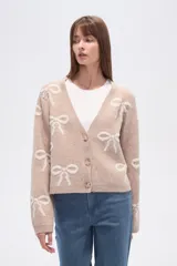 Cárdigan color beige con estampado de moños blancos, escote en V y cierre frontal con botones.