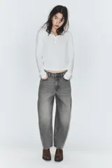 Jeans de tiro medio con diseño cropped, confeccionados en denim gris con efecto lavado. Presentan costuras laterales torcidas, trabillas para cinturón, cinco bolsillos y cierre frontal con cremallera y botón metálico.