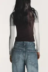 Camiseta de manga larga con diseño de capas superpuestas que crea un efecto triple. Presenta cuello redondo, corte ajustado y combinación de colores en tonos blanco, gris y negro.