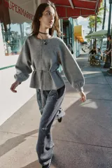 Jersey de punto color gris, con cuello redondo, mangas largas abullonadas con puños elásticos y cintura ajustable mediante cordón. Presenta una costura vertical marcada en la parte frontal.