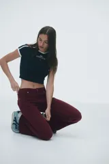 Pantalón de jean color bordó, de tiro bajo, corte ajustado hasta la rodilla y acampanado desde allí hacia abajo. Presenta cierre y botón frontal, bolsillos abiertos delanteros y bolsillos traseros con solapa y botón.