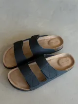 Sandalias negras con dos tiras anchas con costuras en forma de X, plantilla de corcho y suela de goma.