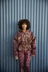 Campera impermeable con capucha y cierre frontal, con estampado de hojas en tonos marrones y ocres. Tiene bolsillos laterales ocultos y cordón ajustable en la cintura.