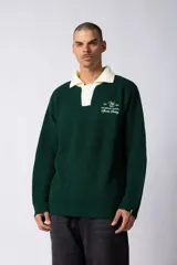 Sweater de punto acanalado en color verde oscuro, con cuello polo en contraste color crema y cierre frontal de botones. Presenta un bordado decorativo en el pecho con texto y logo.