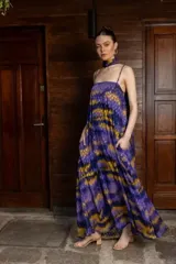Vestido largo de tirantes finos con diseño holgado y bolsillos laterales. Presenta un estampado abstracto en tonos violeta y mostaza, e incluye un accesorio tipo pañuelo para el cuello a juego.