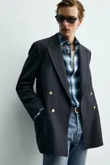 Blazer de corte regular confeccionada en lana, con diseño de botonadura cruzada y solapas de pico. Presenta mangas largas, bolsillos de vivo en el pecho y la cadera, un bolsillo interior y una abertura central en la espalda.
