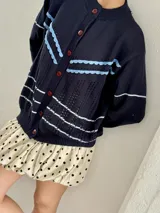 Saco de punto color crema con detalles en crochet verde, cierre frontal con botones y mangas largas.