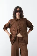 Sobrecamisa de gamuza color marrón, de silueta relajada, con cuello camisero, botones frontales y bolsillos de parche en el pecho.