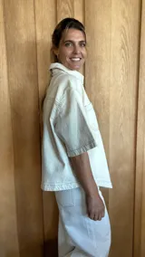 Sobrecamisa de denim soft en tono azul medio, con corte oversize, mangas cortas, cuello clásico y cierre frontal con botones metálicos. Presenta dos bolsillos frontales con solapa y un ruedo redondeado.